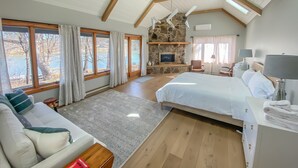 Un dormitorio espacioso con una cama grande, una chimenea de piedra, un televisor y vistas al exterior.