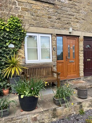 A stone building with a wooden bench, potted plants, and a door with a number plaque. - Lavender Cottage Grewelthorpe Nr Masham Ripon (Ripon)