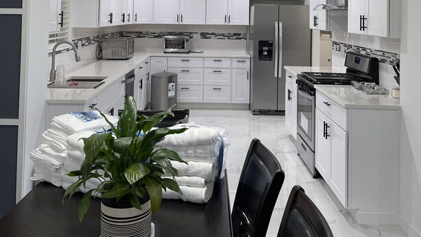 Una cocina moderna con armarios blancos, electrodomésticos de acero inoxidable y una mesa de comedor de madera oscura con sillas.
