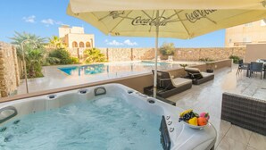 A hot tub with a Coca-Cola branded umbrella, a pool, outdoor seating, and a view of a stone building. - Wellness Hygge Modern Gozitan Apartment (Xaghra)