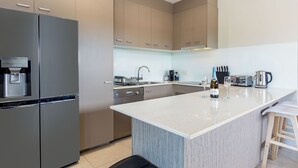A modern kitchen with a stainless steel refrigerator, a coffee machine, a sink, and a bar area with stools. - Awesome, modern, open-plan 3rd floor (with lift) unit with stunning water views. (Bongaree)