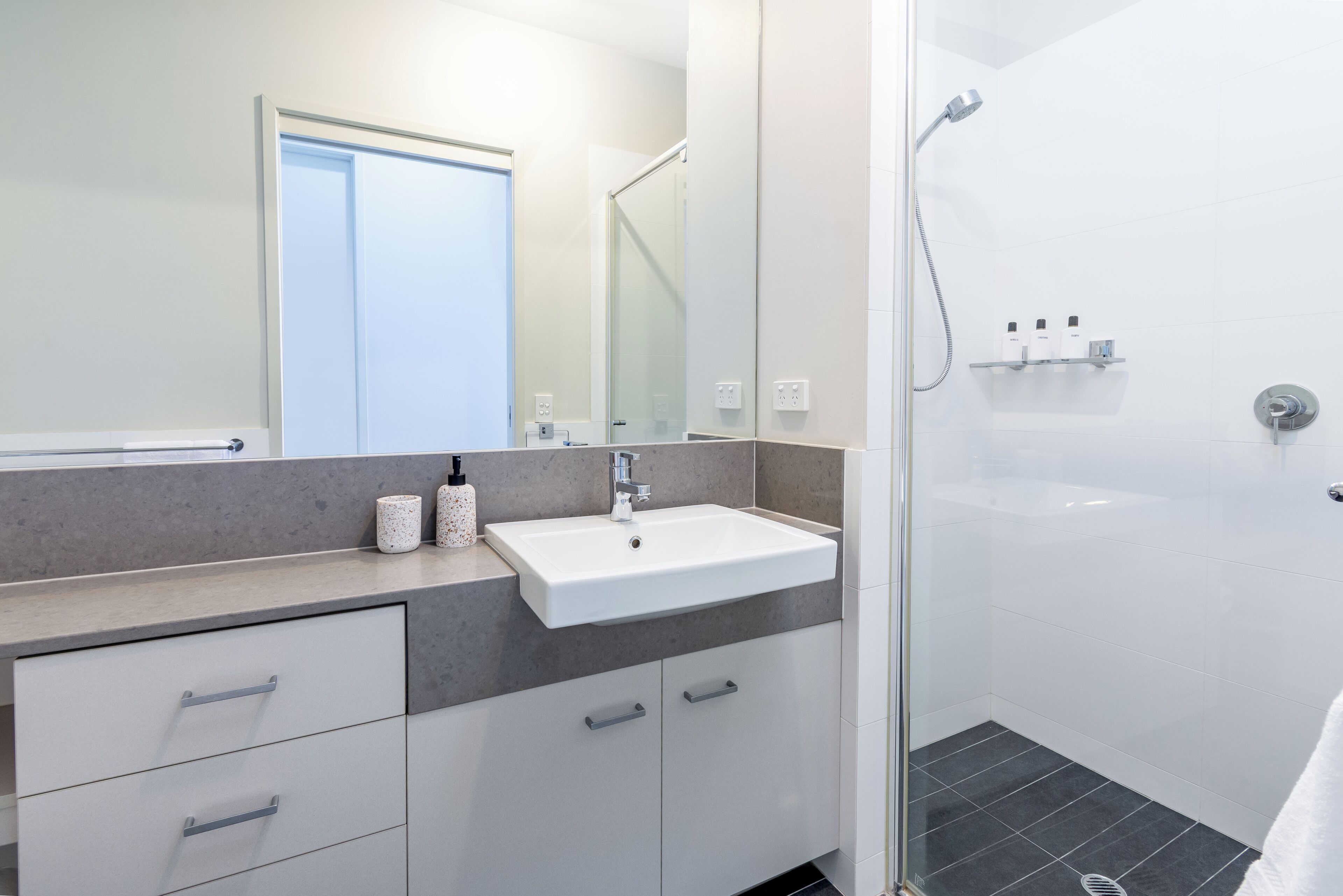 A modern bathroom with a white sink, a glass shower enclosure, and a door leading to another room.