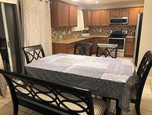 Enjoy meals at the dining table with four chairs, surrounded by a kitchen with a refrigerator and microwave.