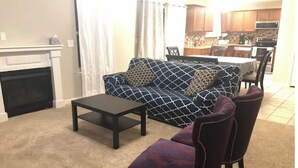 Ein Wohnzimmer mit Kamin, einer Couch, einem Couchtisch und einem Essbereich im Hintergrund.