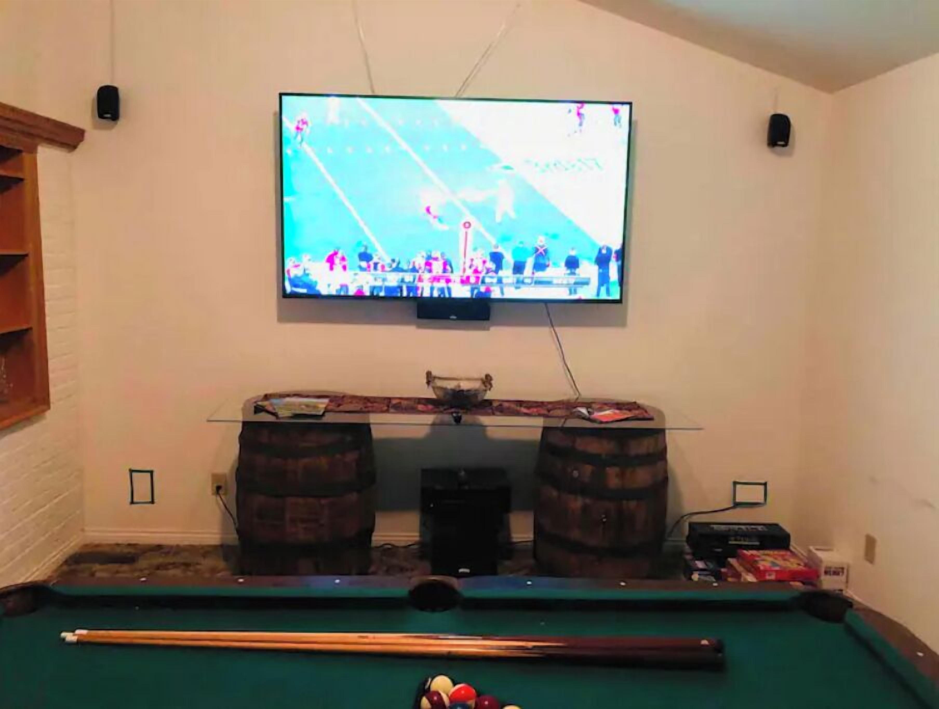 A room with a pool table, a television mounted on the wall, and two wooden barrels.