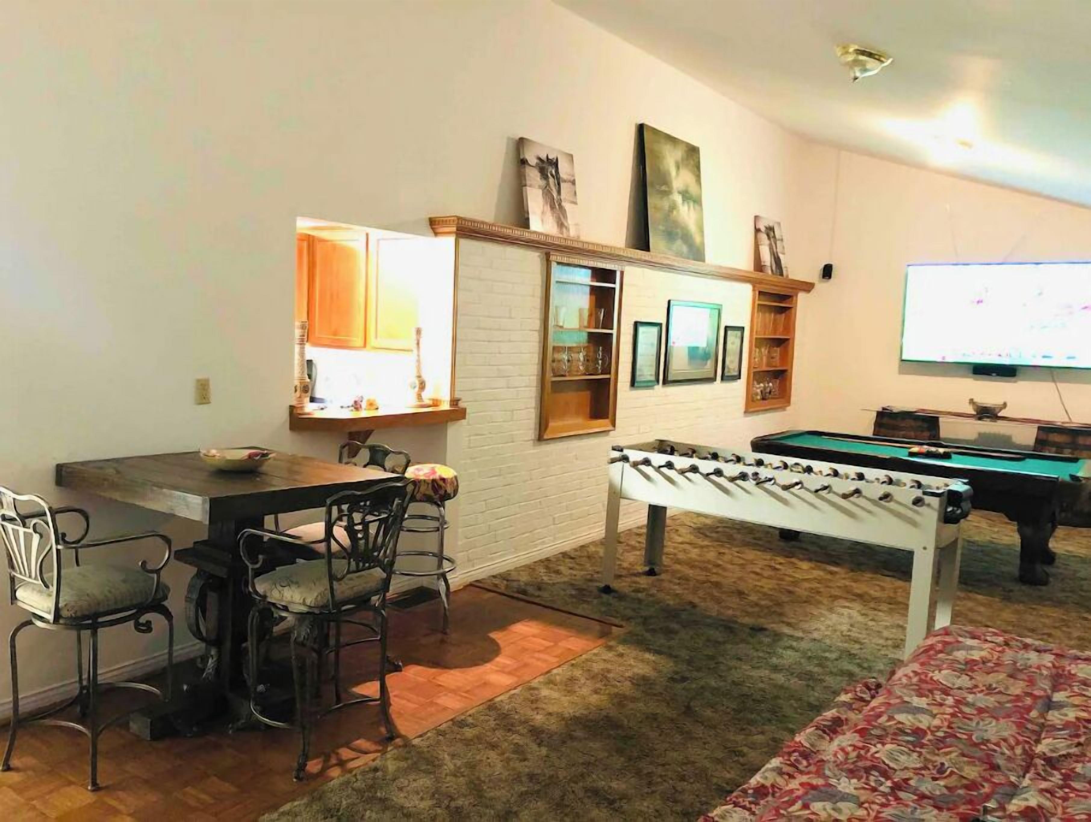 Una sala de estar con mesa de billar, mesa de fútbol y comedor con sillas y una mesa.