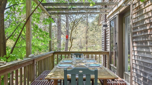 Een houten terras met een eettafel, omringd door bomen.