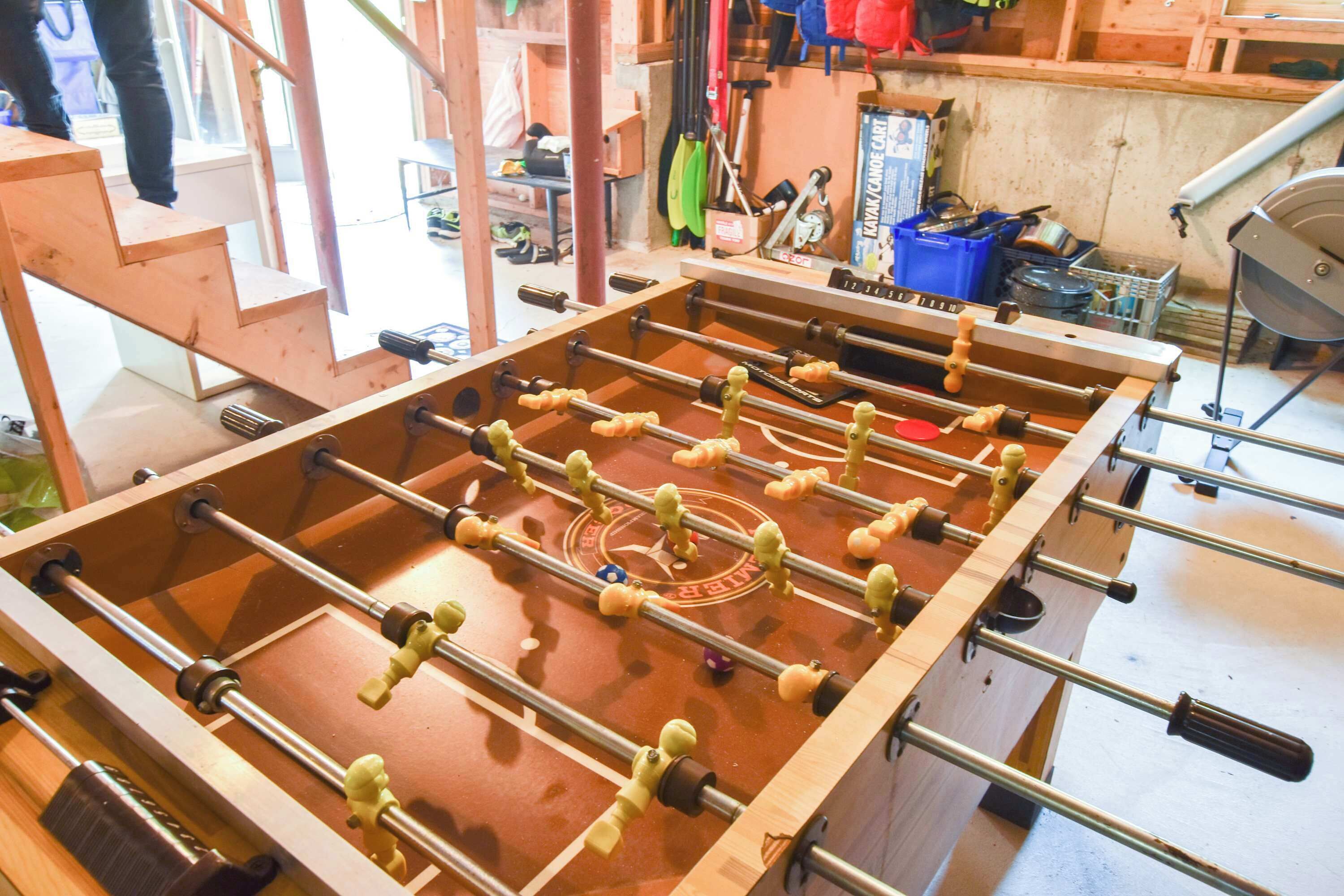 A wooden foosball table in a room with a window, a blue storage bin, and various tools.