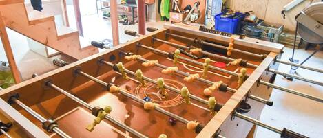 A wooden foosball table in a room with a window, a blue storage bin, and various tools.