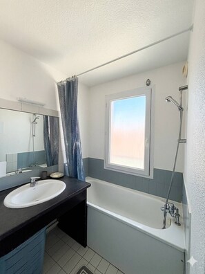 Ein Badezimmer mit Badewanne, Fenster, Dusche, Waschbecken und Spiegel.