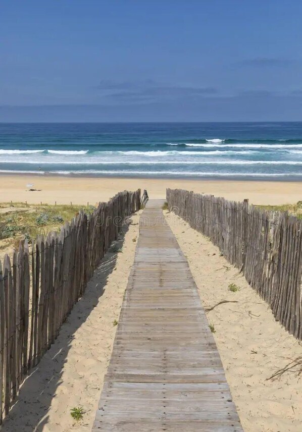 Ein hölzerner Steg führt zu einem Strand mit Blick auf das Meer.