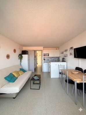 A compact living space with a sofa, dining table, kitchenette, and a TV.