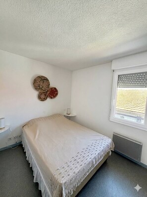 Une chambre à coucher avec un lit, une fenêtre avec des stores, un radiateur et des éléments de décoration murale.