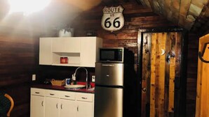 Cuina compacta amb armaris blancs, un frigorífic d'acer inoxidable, un microones i una porta de fusta. Es veu un senyal de Route 66 per sobre dels armaris.