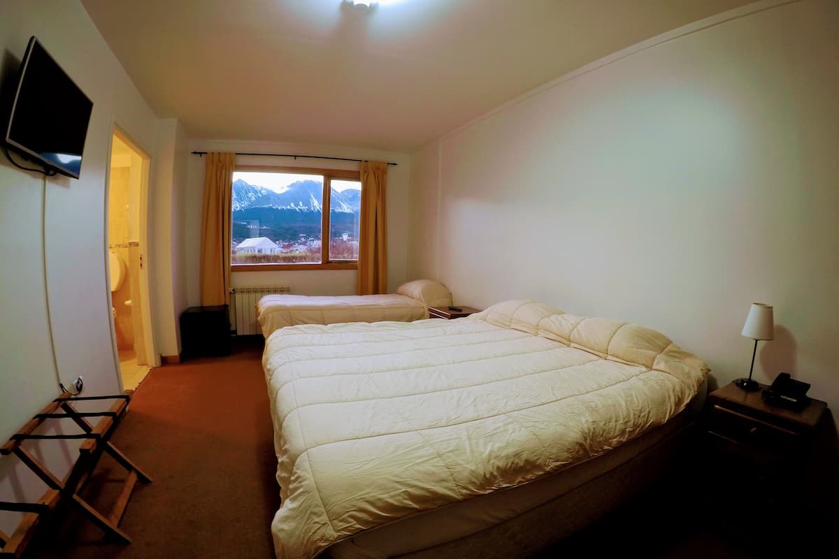 A hotel room with a large bed, a smaller bed, a TV mounted on the wall, and a window with a mountain view.