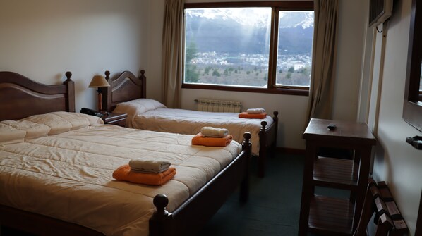 A hotel room with two beds, a small table, a chair, and a window with a view of a mountainous landscape. - Oikos (Ushuaia)