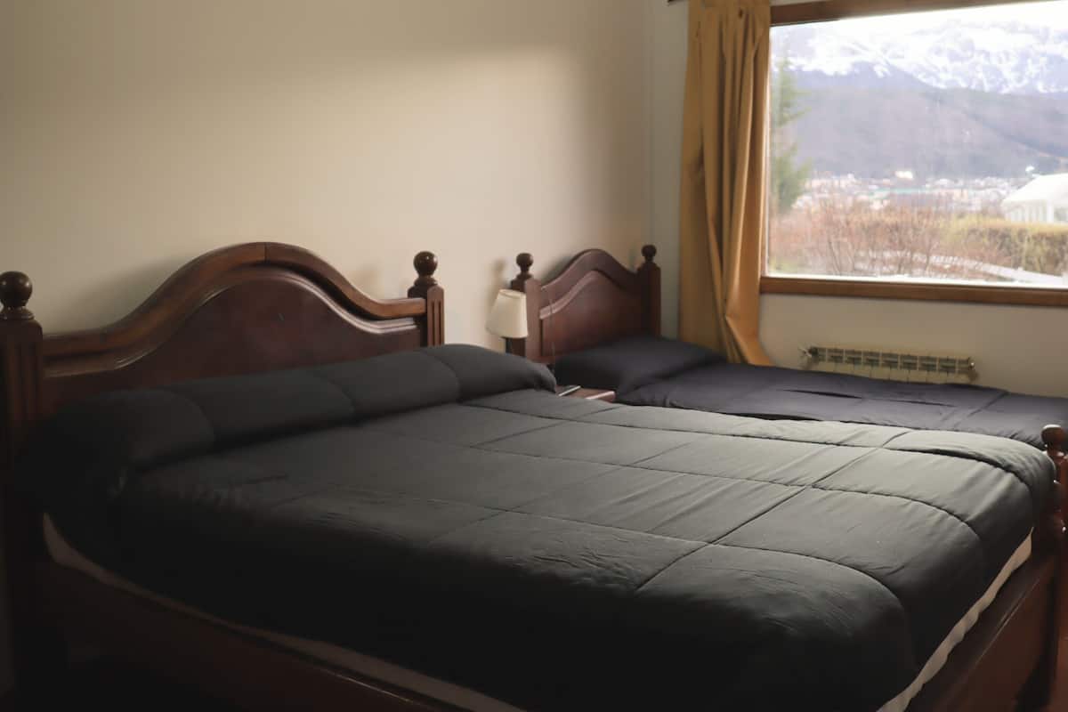 A room with two wooden beds, a window with a view of mountains, and a radiator.