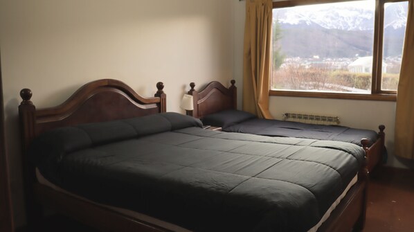 A room with two wooden beds, a window with a view of mountains, and a radiator.