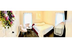 Un dormitorio con una cama, una silla, una mesita y una ventana con cortinas.