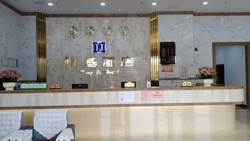 A hotel reception area with a marble wall, a reception desk, a clock, and a digital display.