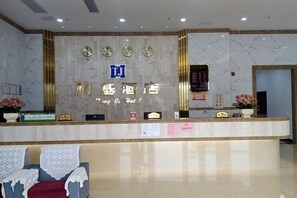A hotel reception area with a marble wall, a reception desk, a clock, and a digital display. - Tengji Hotel (Taishan)