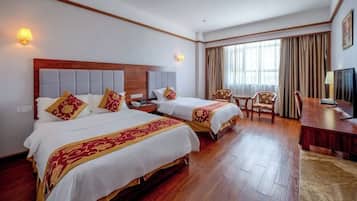 A hotel room with two beds, a desk, a chair, and a television.