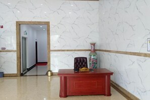 A reception area with a marble wall, a reception desk, and a vase. - Tengji Hotel (Taishan)