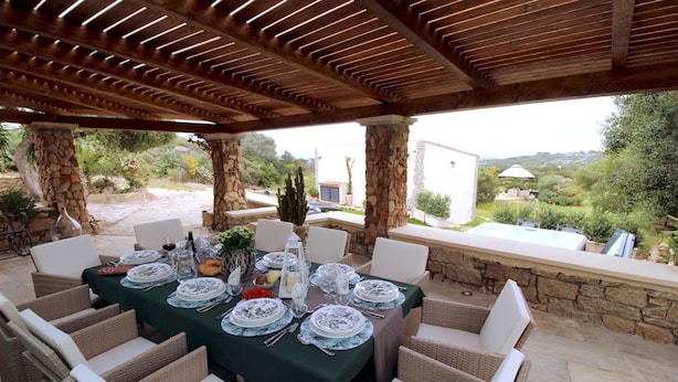 An outdoor dining area with a stone column, wicker chairs, and a table set for a meal.