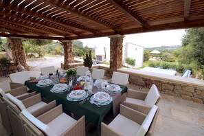 Un espacio al aire libre para comer con un pilar de piedra, sillas de mimbre y una mesa dispuesta para una comida.