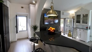 A modern kitchen with a large island, a hanging pendant light, and a bowl of oranges on the counter.