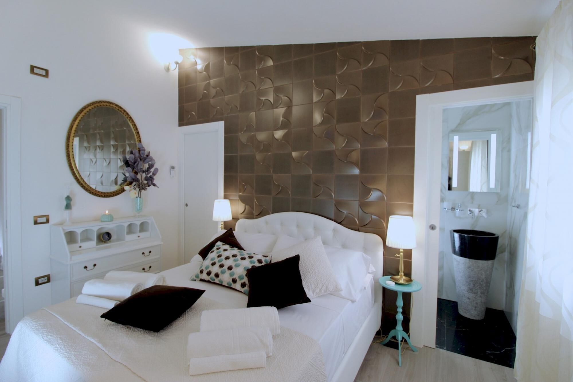 Ein ordentlich bezogenes Bett mit Kissen, ein Nachttisch mit Lampe, ein Spiegel und eine Wand mit dekorativem Wandpaneel.
