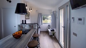 A modern kitchen with a wooden island, bar stools, a bowl of oranges, pendant lighting, and a view of greenery outside.