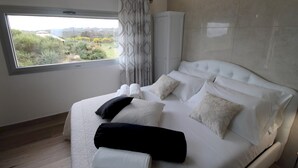 A modern bedroom with a large bed, a view of greenery outside, and a window with curtains.