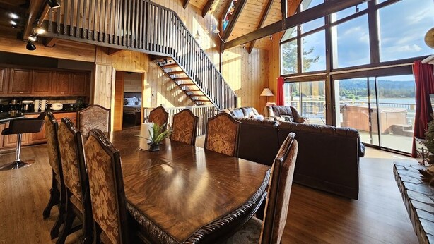 A spacious living area with a wooden staircase, large windows, and a dining table. - Romantic Sunset Lakefront View, Minutes to the Slopes and Village! (Big Bear Lake)