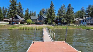 A wooden dock extending into a calm body of water, surrounded by residential buildings with large windows and balconies, set against a backdrop of tall trees. - Romantic Sunset Lakefront View, Minutes to the Slopes and Village! (Big Bear Lake)