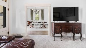 Un salon avec un canapé en cuir, un meuble TV en bois foncé et, au fond, un coin repas.
