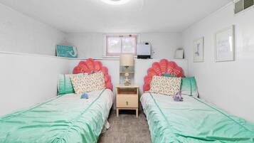 Quarto com duas camas de solteiro, mesa de cabeceira, luminária, janela e decorações nas paredes.