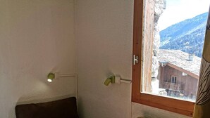A corner room with a brown sofa, a window with a view of a mountain, and a wooden door. - La Clairière 1 - Nice divisible studio with a mountain view (LES AVANCHERS VALMOREL)