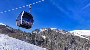 A cable car labeled "VALMOREL 2" suspended over a snowy mountain landscape with dense forests.