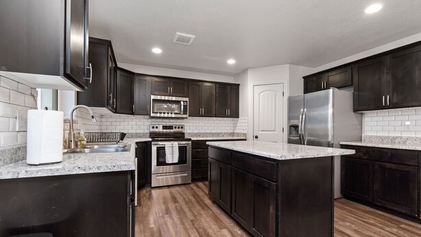 A modern kitchen with dark cabinets, stainless steel appliances, and a white tiled backsplash.