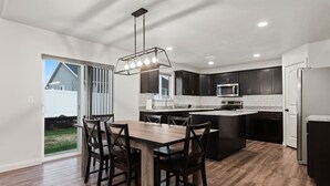A modern kitchen with a dining area, featuring dark cabinetry, a central island, and a large window.