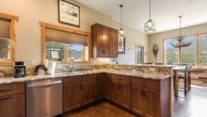 A modern kitchen with wooden cabinets, a built-in dishwasher, and a granite countertop. - Show Me Mountain Views -- 20-ncd0130 3 Bedroom Home by RedAwning (Estes Park)