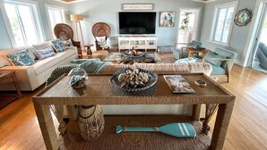 Un salón amplio con techo de madera, un televisor de pantalla plana grande y un rincón de estar acogedor con un sofá y sillones.