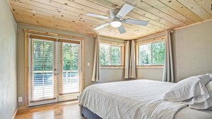 Un dormitorio con cama, techo de madera, ventilador de techo y ventanas grandes con cortinas.