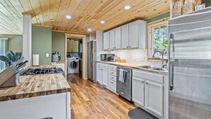 Una cocina moderna con suelo de madera, armarios grises, electrodomésticos de acero inoxidable y un área de lavandería a la vista.