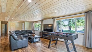 Amplia sala de estar con sofá de cuero, mesa de futbolín y televisor.