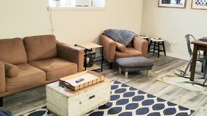 A living room with a brown sofa, a small table, a coffee table with a tray, a patterned rug, and a ceiling fan.