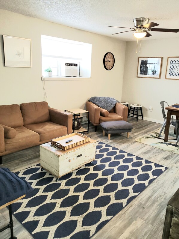 A living room with a brown sofa, a small table, a coffee table with a tray, a patterned rug, and a ceiling fan.