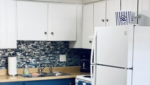 A kitchen with white cabinets, a blue countertop, a white refrigerator, and a patterned backsplash.