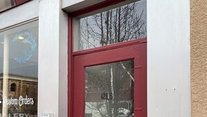 A red door with a window above it, a keypad lock, and a sign that reads "Custom Orders".